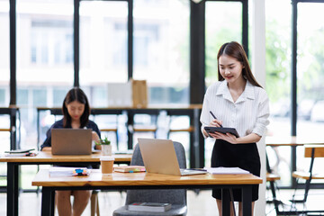 Portrait of young Asian businesswoman in suit, woman smiling and work at workplace inside office, accountant with calculator behind paper phone signing contracts and financial reports
