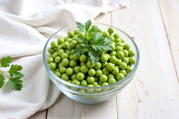 Glass bowl green peas parsley sprig wooden surface natural light