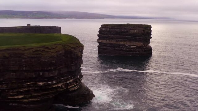 Aerial push in reveals Dun Briste sea stack off Downpatrick Head cliffs in Ireland, wide view under cloudy sky