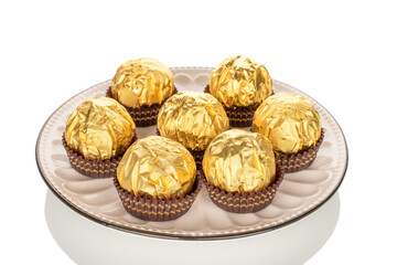 Several chocolate candies wrapped in gift paper with ceramic dishes, close-up, isolated on white background.