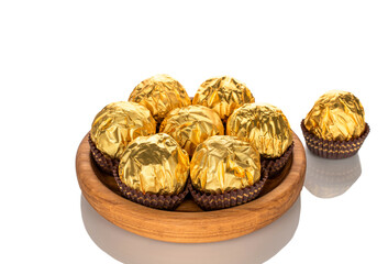 Several chocolate candies wrapped in gift paper with wooden utensils, close-up, isolated on white background.