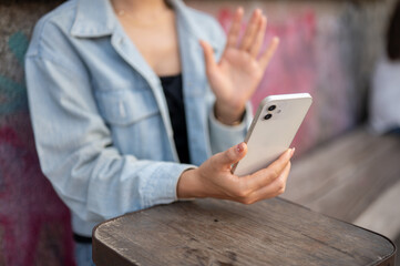A woman sits at an outdoor table of a cafe, using her smartphone, talking on a video call.