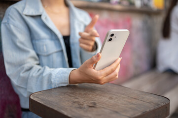 A woman sits at an outdoor table of a cafe, using her smartphone, talking on a video call.