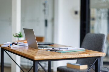 Laptop Computer, notebook, and eyeglasses sitting on a desk in a large open plan office space after...