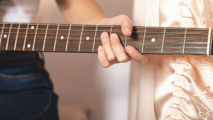 Close-up of a women playing a guitar on a bed. Guitar strings visible. Relaxed atmosphere with an emphasis on music. A woman plays an electric guitar.
