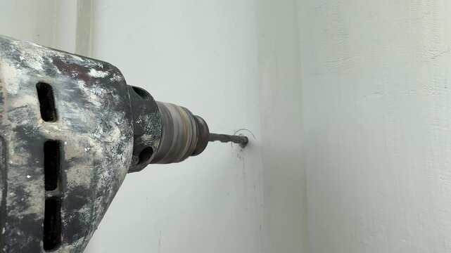 4k footage, carpentry works drilling a hole for screw and wall plugs inside the solid wall. Close up of electric driller drilling a hole on a white wall, as part of carpentry installation process.