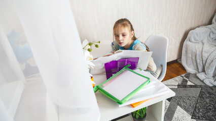 Little school girl sit at table at home write in exercise book prepare homework alone.