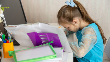 Little school girl sit at table at home write in exercise book prepare homework alone.