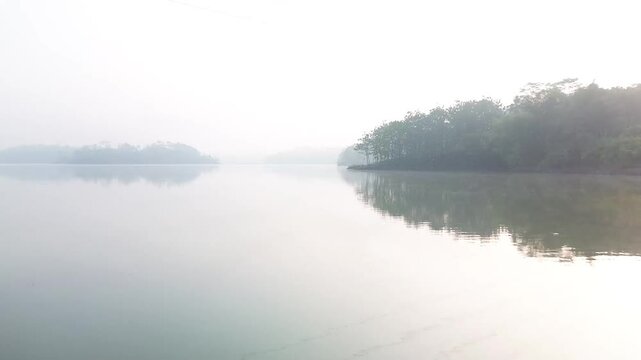 4k footage of a lake with calm water in the morning, covered in a thin mist
