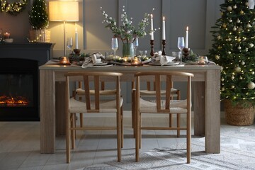 Christmas table setting with stylish dishware, glasses and burning candles in festive decorated room