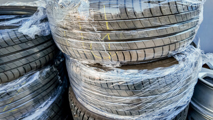 Stacks of brand-new car tires wrapped in plastic, highlighting transportation safety, maintenance,...