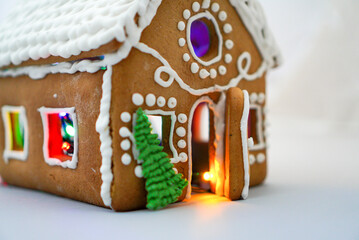 A handmade decorated gingerbread Christmas house photographed close-up on a white background with Christmas lights and bokeh.