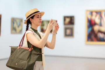 Mid shot of young Caucasian beautiful woman in an elegant clothes and straw hat takes photo with...