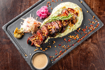 A beautifully plated dish featuring tender grilled meat on a bed of creamy mashed potatoes, garnished with herbs, pickled vegetables, and a rich sauce on the side. Perfect for food lovers.