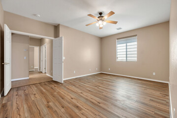 Spacious empty room with wooden flooring and ceiling fan in a residential setting