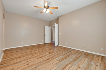 Spacious empty room with wooden flooring and ceiling fan in a residential setting