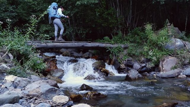 Backpacking couple cross small forest stream on rickety log bridge