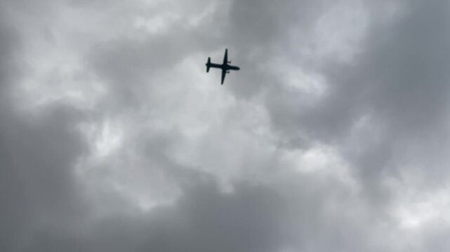 Silhouette of propeller aircraft passing in the sky seen from below with overcast cloudy background during the day.