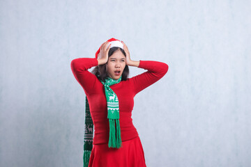 Asian adult woman with left side headache with both hands holding head, wearing christmas sweater party wear, Santa hat and scarf, isolated on white background