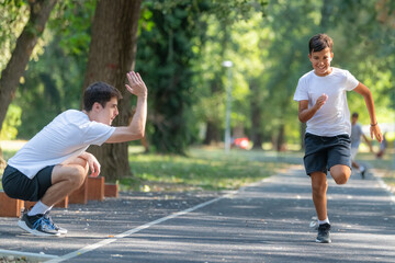 Trainer helps a young boy practice speed running in a park, focusing on technique and fitness. The natural setting  