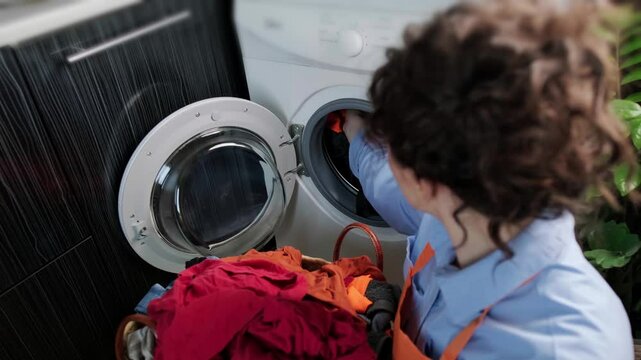 Woman places a laundry capsule into the washing machine drum and closes the door, using detergent pods with fabric softener for washing.