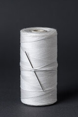 White thread spool with needle close-up flat lay top view on black background with copy space for text