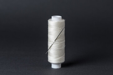 White thread spool with needle close-up flat lay top view on black background with copy space for...