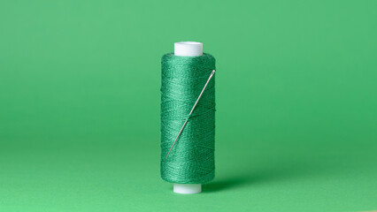Green thread spool with needle close-up flat lay top view background with copy space for text