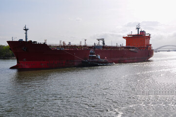 Tugboat assisting a large tanker ship in navigating a river