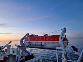 Lifeboat hanging from davit on ferry at sunset
