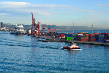 Fototapeta premium Tugboat navigating a busy port with cargo and cruise ship