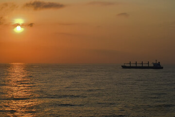 Serene Sunset Over Ocean with Cargo Ship Silhouette