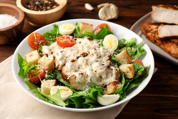 Tasty Caesar salad with chicken and tomatoes in bowl on wooden table, closeup