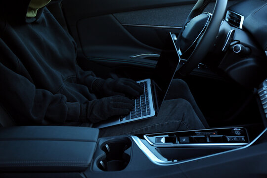 Thief hacking car system with laptop inside vehicle, closeup
