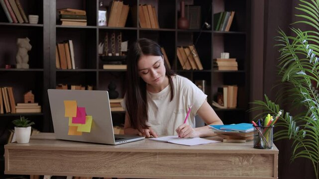 Young woman student makes notes while looking at laptop