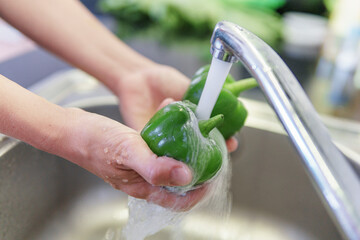 Woman hands washing fresh green bell pepper in kitchen
