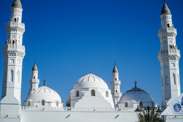 A stunning view of a pristine white Quba mosque, its minarets reaching towards a vibrant blue sky....