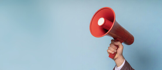 Hand holds a red megaphone isolated on blue background. Concept of communication, message, announce