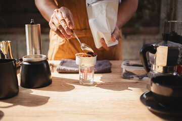 Barista is grinding coffee beans with manual stainless steel grinder to make black coffee machine, brewing equipment or coffee drip set Dripper on a wooden table In the kitchen at home in the morning.