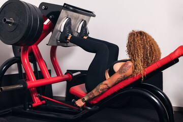 unrecognizable sportswoman with curly hair doing exercises on leg press machine in gym, concept of fitness and active lifestyle