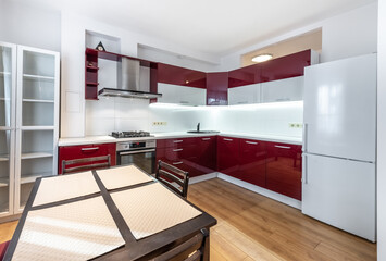 Scandinavian Style Cozy Modern Kitchen with Red and White Cabinets and Dining Area. Home Interior. Faucet, Fridge, Oven, Closet and Furniture in Background.