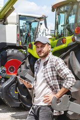 Male farm worker with digital tablet against tractor at agricultural equipment dealership.