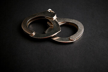 Steel handcuffs lying on a dark background, representing concepts of crime, arrest, law...