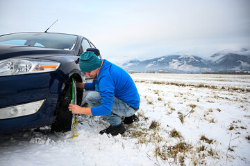 Man installing snow chains on car tire during winter, ensuring safety on snowy roads