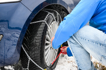 Man installing snow chains on car tire during winter, ensuring safety on snowy roads