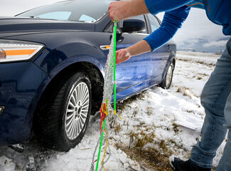 Man installing snow chains on car tire during winter, ensuring safety on snowy roads
