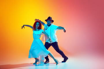 Practicing lively steps of salsa, duo perfects their rhythm and synch in neon light against...