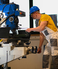 Factory worker operating a milling machine, demonstrating workplace safety with proper attire and...