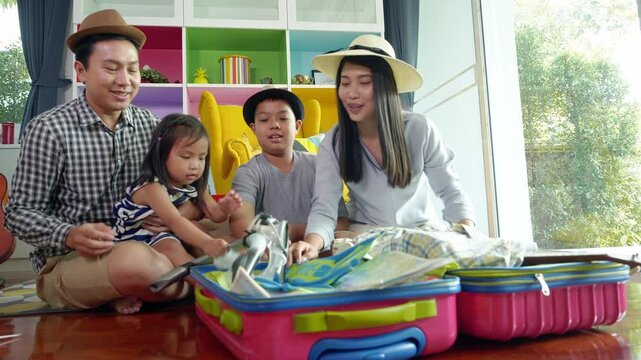 Happy Asian family enjoy packing clothes and accessories into luggage at home before their going to travel.