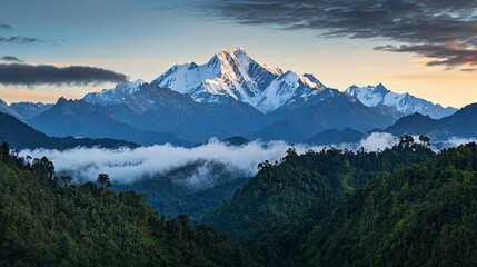 Obraz premium A breathtaking mountain range rises above lush forests and clouds, illuminated by a soft sunrise.
